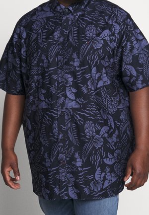 Short-sleeve button-up shirt with dark blue and purple tropical floral and leaf patterns worn by a person.