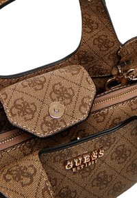 Pochette marrone Guess con motivo monogram, zip in tonalità oro, bottone a scatto e logo in metallo "Guess Est 1981" sulla tasca anteriore.