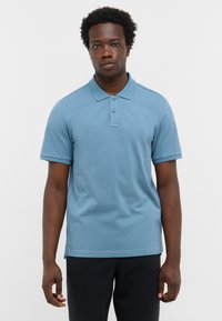 Jasnoniebieska koszulka polo z teksturowanej tkaniny, z kołnierzykiem, trzema guzikami i krótkimi rękawami. Małe logo na piersi.