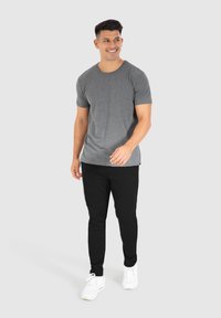 Graues Kurzarm-T-Shirt mit lässiger Passform, kombiniert mit schwarzen Jogginghosen und weißen Sneakers, vor einem neutralen Hintergrund.