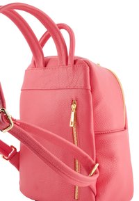 Sac à dos en cuir texturé rose avec des poignées courtes, une bandoulière ajustable, des fermetures éclair dorées et une poche zippée extérieure. Forme arrondie.