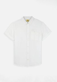 Chemise blanche à manches courtes avec un col, dotée d'une poche poitrine et d'un motif à pois à l'intérieur du col. Texture de tissu douce.