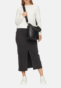 Borsa a spalla in pelle nera con tracolla regolabile, forma squadrata, design minimalista, indossata con un maglione bianco strutturato e una gonna di jeans nera.