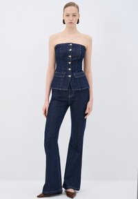 Top peplum in denim con design senza spalline, caratterizzato da bottoni dorati sulla parte anteriore e due tasche. Abbinato a pantaloni in denim a campana.