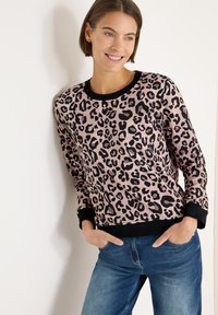 Bluza w panterkę z miękkiego materiału. Posiada czarne ściągacze przy mankietach i dekolcie. Połączona z niebieskimi dżinsami, lekka konstrukcja odpowiednia na codzienne noszenie.