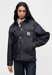 Σκούρο τζιν μπουφάν με άνετη εφαρμογή, διαθέτει δύο τσέπες στο στήθος, χρυσά κουμπώματα και ορατό λογότυπο. Συνδυάζεται με πουκάμισο με γιακά.