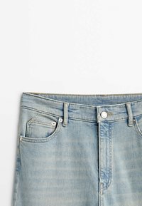Jean en denim bleu clair, présenté de la taille au milieu de la cuisse avec fermeture à boutons et poches avant sur fond blanc.