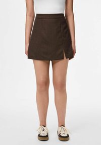 Mini gonna a righe marroni con vita aderente e una fessura frontale, realizzata in un tessuto liscio. Abbinata a scarpe da ginnastica casual con lacci.