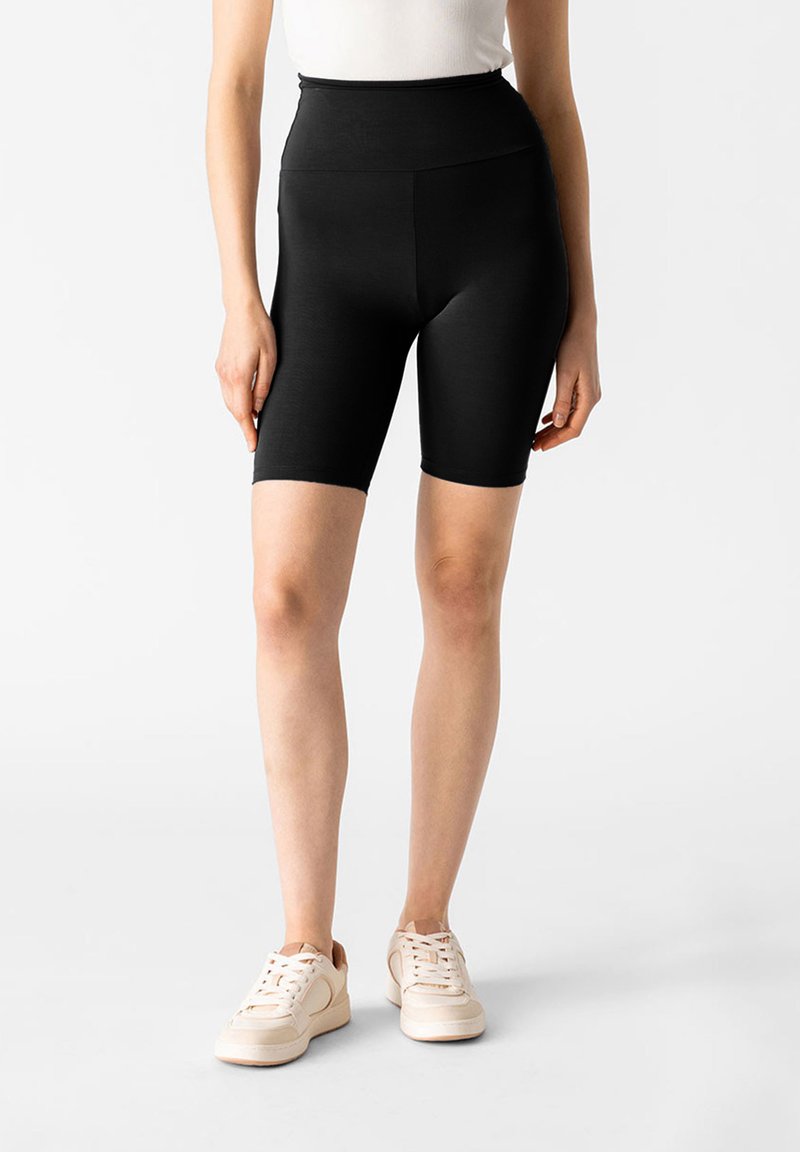 Shorts da ciclismo neri a vita alta realizzati in tessuto elasticizzato, con una finitura liscia e un design lungo fino al ginocchio, abbinati a sneakers leggere.