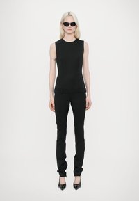 Haut sans manches noir associé à un pantalon noir ajusté, en tissu lisse, complété par des talons aiguilles noirs et des lunettes de soleil sombres.