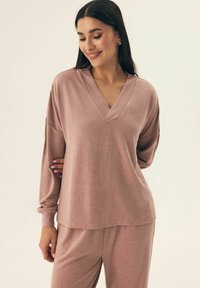 Jasnoróżowy sweter z długim rękawem i dekoltem w kształcie litery V, wykonany z miękkiej tkaniny, z opadającymi ramionami i prążkowanymi detalami przy dekolcie i mankietach.