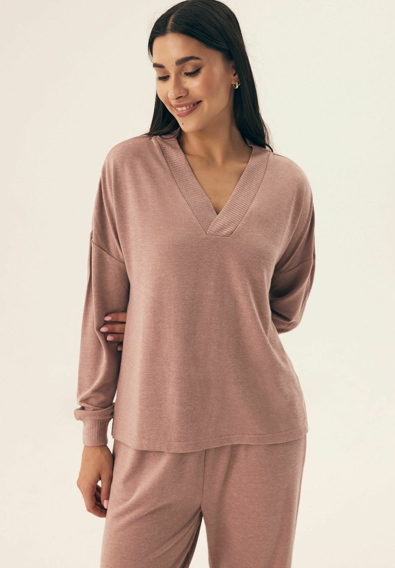 Jasnoróżowy sweter z długim rękawem i dekoltem w kształcie litery V, wykonany z miękkiej tkaniny, z opadającymi ramionami i prążkowanymi detalami przy dekolcie i mankietach.