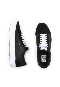 Baskets Vans noires avec semelles blanches et lacets blancs, présentées de côté et par le dessus sur un fond blanc.