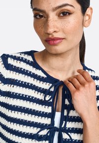 Knit cardigan with navy and cream horizontal stripes, featuring a tie closure at the neck and open stitch details for breathability.