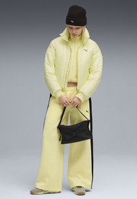 Puffjacka och matchande träningsoverall i ljusgul, med svarta sidostr�äck och logotyp. En svart handväska och beige sneakers fulländar looken.