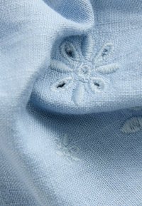 Tessuto di un blu chiaro con una texture morbida presenta motivo floreale ricamato. Il design include piccoli ritagli e dettagli delicati.
