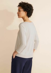 Maglietta beige chiaro a maniche lunghe con scollo rotondo, caratterizzata da una texture liscia e un fitting rilassato, abbinata a pantaloni blu navy.