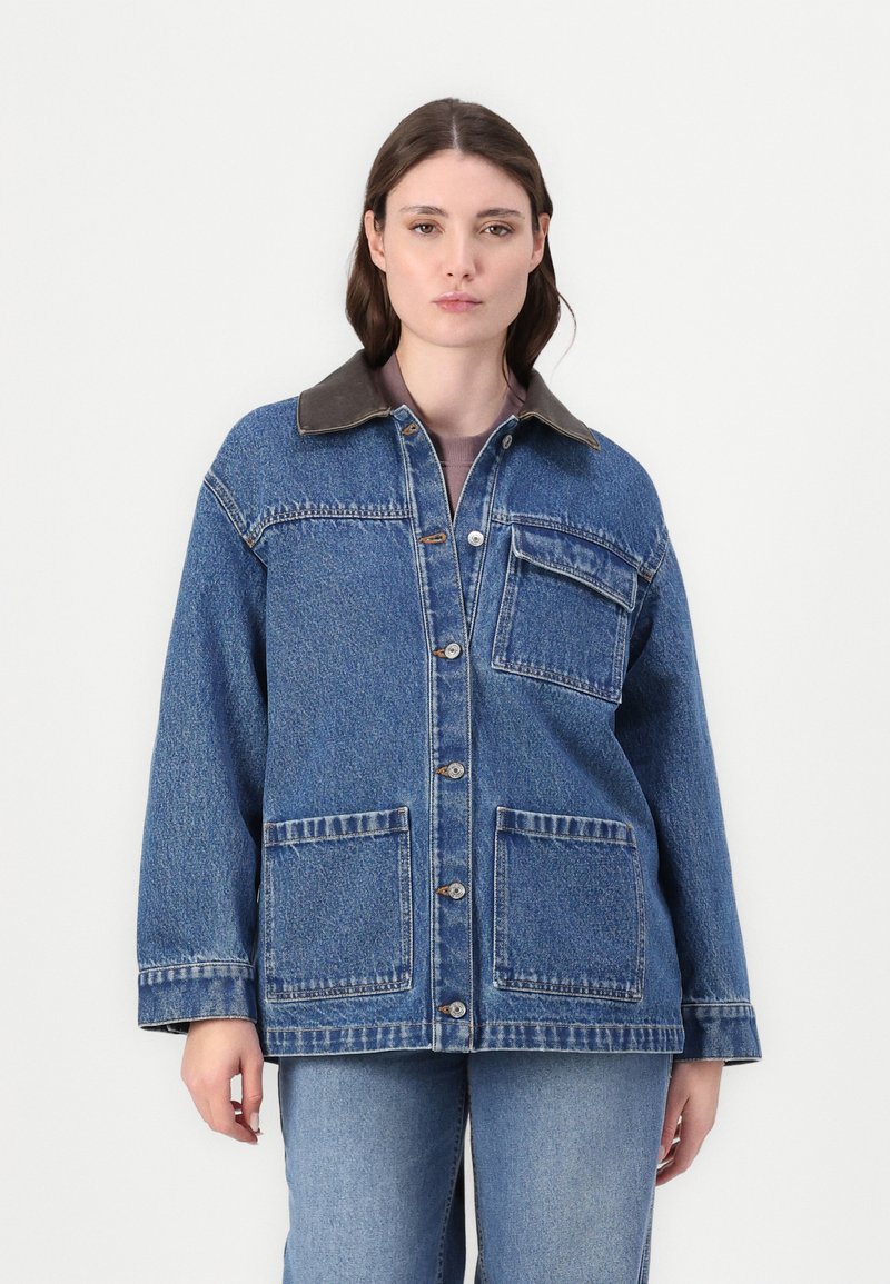 Jeans jakna v modri barvi z rjavim žametnim ovratnikom, sprednjim gumbom, dvema velikima sprednjima žepoma in enim žepom na prsih. Oprijet kroj.