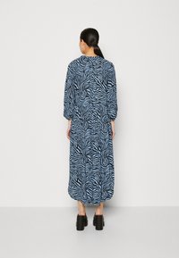 Robe maxi à rayures zèbre bleues et noires, fabriquée dans un tissu léger. Comprend des manches longues, une taille élastique et une coupe décontractée.