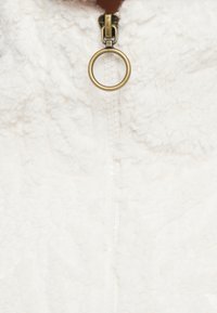 Biela flísová látka s jemnou textúrou, vybavená zlatým zipsom s okrúhlym ťahadlom na golieri.