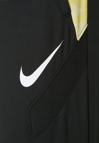 Schwarze Sporthose von Nike mit einem weißen Logo, Seitentasche und gemustertem gelben Akzent. Hergestellt aus glattem, strapazierfähigem Material mit strukturierten Details.