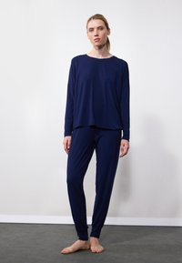 Navy blue loungewear setti, joka sisältää pitkähihainen yläosan, joka on löysä malli, sekä vastaavat kapeat housut, valmistettu pehmeästä ja sileästä kankaasta.