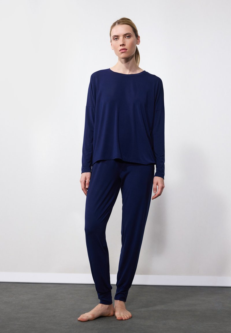 Navy blue loungewear setti, joka sisältää pitkähihainen yläosan, joka on löysä malli, sekä vastaavat kapeat housut, valmistettu pehmeästä ja sileästä kankaasta.