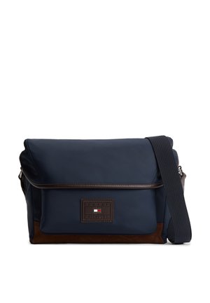 Marineblauwe Tommy Hilfiger boodschappentas met verstelbare zwarte riem, bruine rand en een logopatch aan de voorkant.