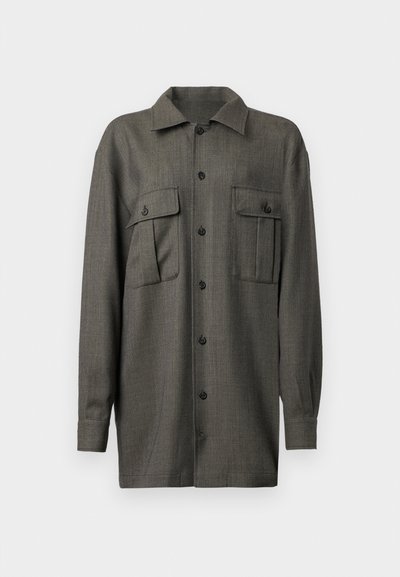 Camisa de botones de manga larga gris oscuro con dos bolsillos frontales con solapa y cuello puntiagudo, exhibida sobre un fondo blanco.