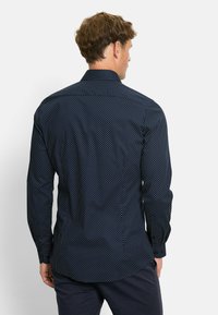 Donkerblauwe shirt met witte stippen, met knopen-kraag, lange mouwen en een gebogen zoom. Gladde stoftextuur met een getailleerde pasvorm.