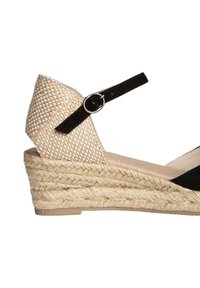 Sandalia de cuña con tira en el tobillo de ante negro, con parte superior de tejido beige, suela de yute y diseño texturizado. Presenta un acento de hebilla redonda de color plateado.