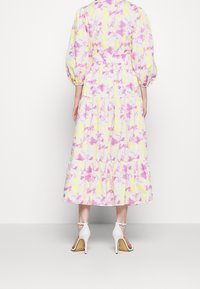Abito lungo a più strati in un motivo astratto pastello giallo e rosa. Presenta maniche a palloncino e una vita aderente. Indossato con scarpe con tacco alto bianche.