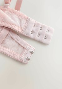 Bretele de sutien roz din dantelă, cu închizători duble cu cârlig și ochiuri pe un fundal deschis, evidențiind textura și detaliile cusăturii.