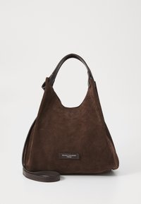 Bruine suède handtas met een zachte textuur, met een gebogen silhouet, korte leren handvatten en een logo plaatje nabij de basis.