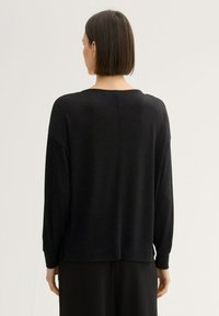 Schwarzer Rundhalsausschnitt-Pullover mit lockerer Passform, überschnittenen Schultern und gerippten Bündchen. Weicher Stoff mit subtiler glänzender Oberfläche, designed für Komfort und zum Layering.