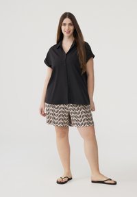 Camicia nera a maniche corte con bottoni abbinata a pantaloni beige con motivo a foglie nere, completata da ciabatte nere.