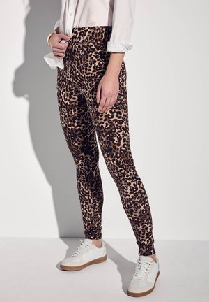 Leopardenmuster Leggings aus dehnbarem Material, das ein figurbetontes Design mit hoher Taille und schmal zulaufenden Beinen zeigt. Kombiniert mit weißen Turnschuhen.