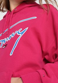 Felpa hot pink con logo frontale in bianco e blu, dotata di cappuccio con lacci e polsini a coste. Realizzata in tessuto morbido e testurizzato.