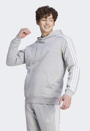 Felpa grigia con strisce bianche sulle maniche, tasca a marsupio e polsini a costine. Presenta il logo Adidas sul petto e pantaloni abbinati.