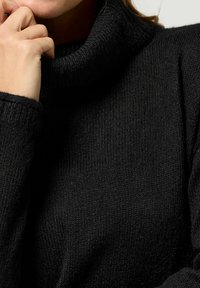 Maglione nero a collo alto in tessuto a maglia texture, con collo alto, maniche lunghe e vestibilità morbida. Dettaglio ravvicinato del tessuto.