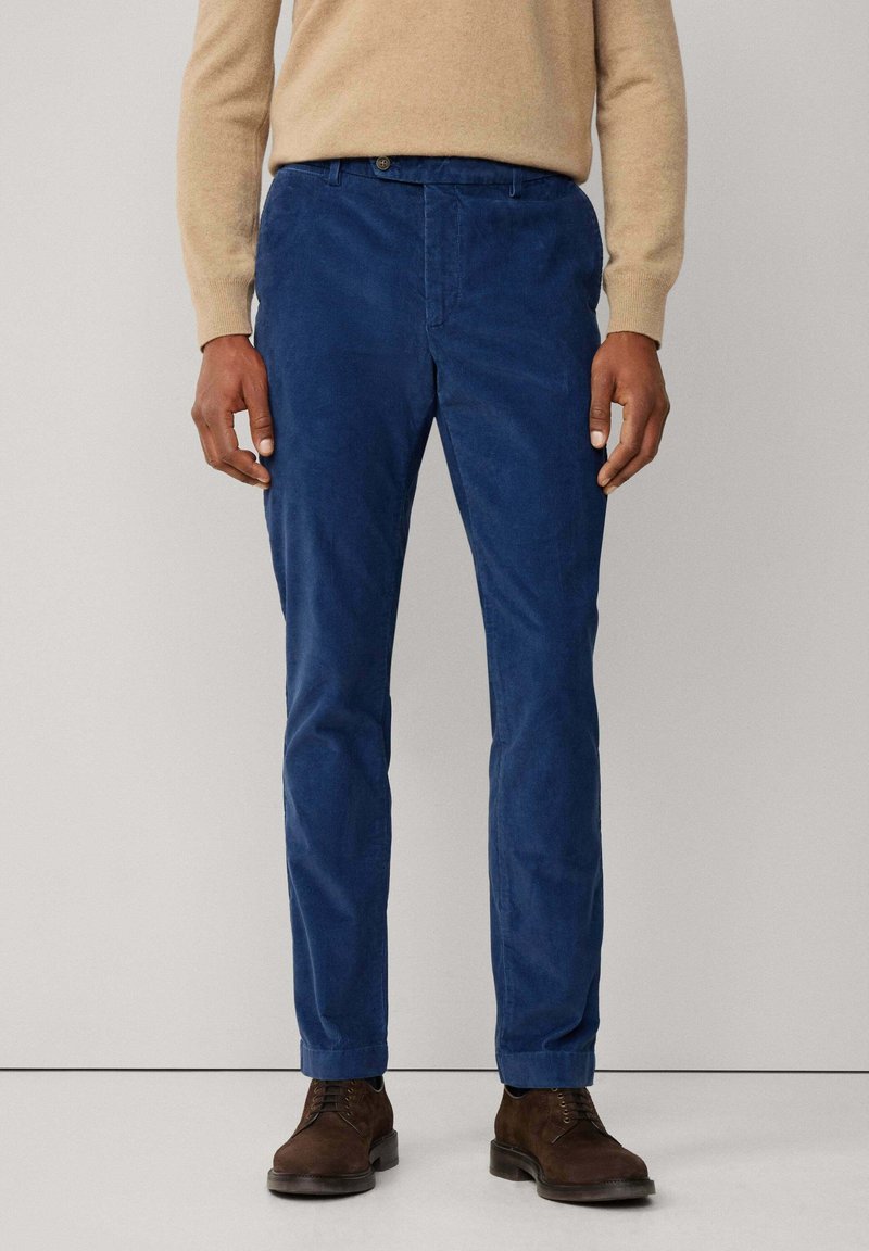 Pantaloni blu in corduroy con design a gamba dritta, caratterizzati da una chiusura con bottone, una texture sottile e orlo ripiegato. Abbinati a scarpe marroni.