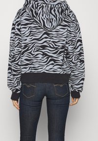 Hoodie accorciato in stampa zebra nera e blu chiaro, con maniche lunghe e cappuccio con cordino. Polsi e orlo a coste neri.