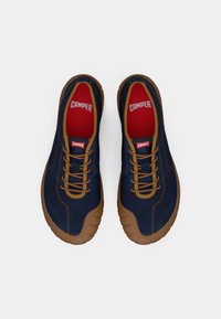 Baskets en daim bleu marine avec des semelles en caoutchouc marron, dotées de lacets beiges et d'une semelle intérieure rouge avec le logo "CAMPER" sur la languette et le talon.