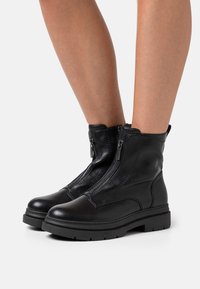 Bottines en cuir noir avec un bout arrondi, des fermetures éclair sur le côté et une finition texturée. Dotées d'une semelle épaisse et robuste ainsi que de coutures renforcées.