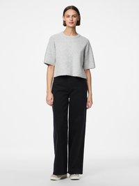 Hall hallatud kampsun ümarate kaeluse ja lühikeste varrukatega, kombineeritud kõrge vöökohaga mustade laia säärega teksade ning heledate kingadega.