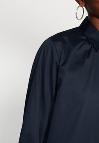 Marineblauwe shirt met een klassieke kraag, een gladde textuur en een licht oversized pasvorm. Het heeft een minimalistisch ontwerp zonder zichtbare patronen.