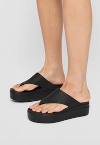 Sandali platform neri con un ampio design a striscia incrociata. Realizzati in materiale liscio, presentano una suola spessa e una silhouette naturale del piede.