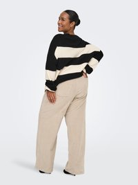 Mustade ja kreemikasvalgete triipudega ülisuur kampsun pikkade varrukatega, mida on kombineeritud laiade jalgadega beežide korduroopükstega. Sile tekstuur, vaba ja lõõgastav istuvus.