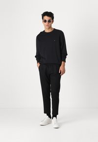 Felpa nera e pantaloni jogger coordinati, realizzati in tessuto morbido. Sneakers bianche e occhiali da sole rotondi completano l'outfit. Branding minimale visibile.