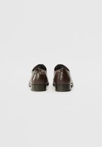 Scarpe in pelle marrone con una superficie liscia, tacco basso e design a punta rotonda. Presentano cuciture sottili e un'estetica minimalista.